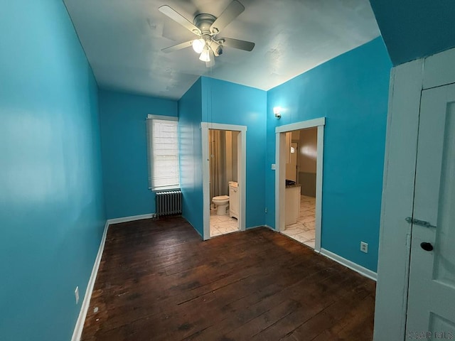 unfurnished bedroom featuring a ceiling fan, baseboards, radiator, hardwood / wood-style floors, and ensuite bath