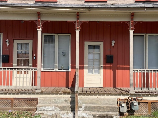 entrance to property featuring covered porch and roof with shingles