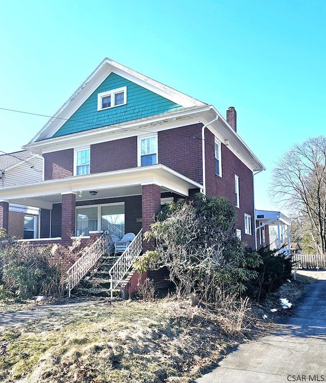 traditional style home with covered porch, brick siding, and a chimney