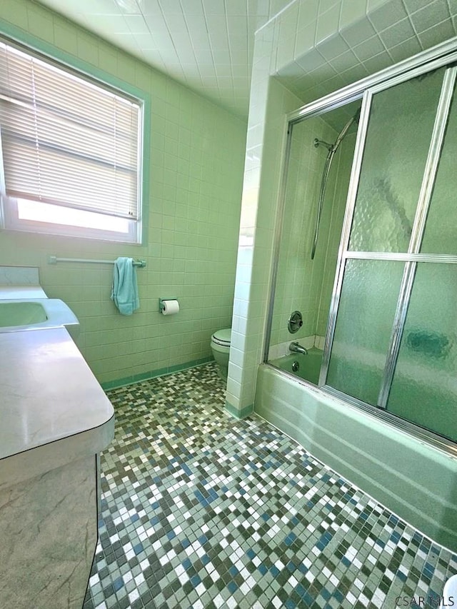 bathroom with enclosed tub / shower combo, toilet, vanity, tile walls, and tile patterned floors