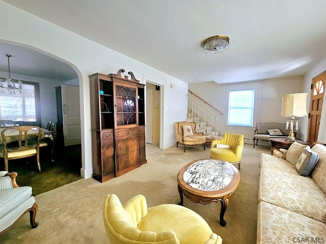 carpeted living area with a chandelier, stairway, and arched walkways