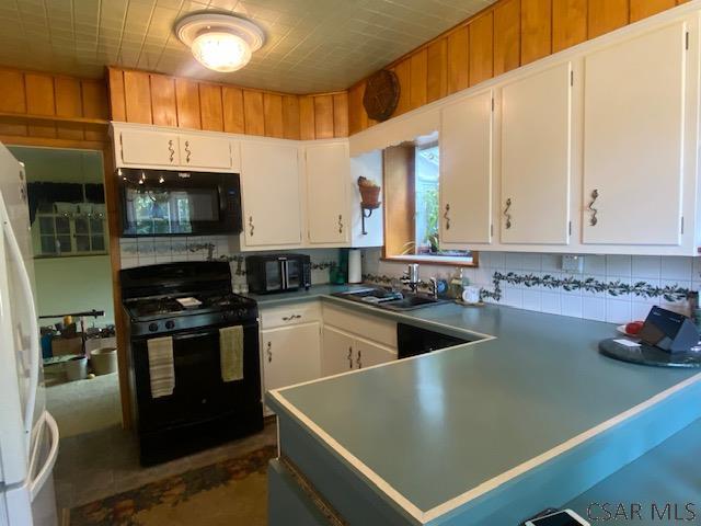 kitchen with white cabinets, kitchen peninsula, sink, and black appliances