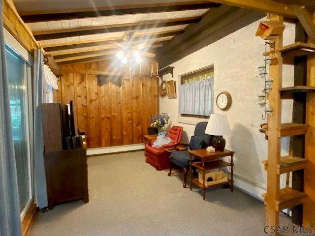 living area featuring a baseboard heating unit, vaulted ceiling with beams, and wood walls