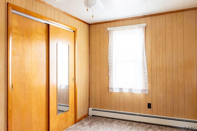 empty room featuring plenty of natural light, a baseboard heating unit, ceiling fan, and wood walls