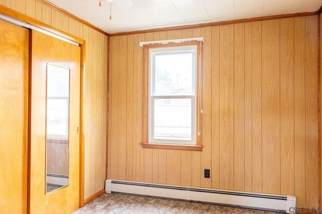 spare room featuring ceiling fan, wood walls, and a baseboard heating unit