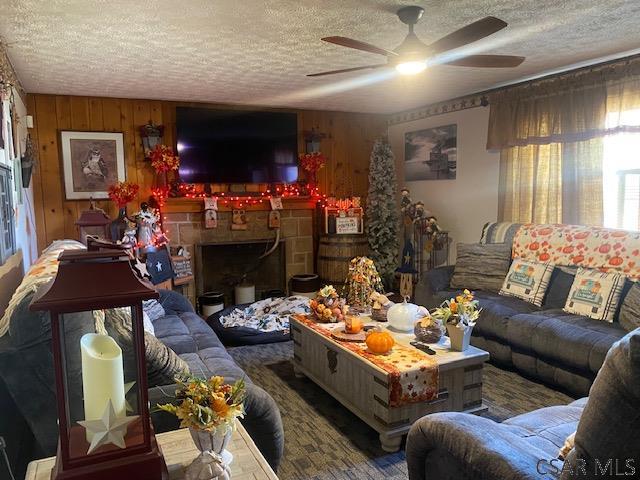 living room with ceiling fan, wooden walls, and a textured ceiling