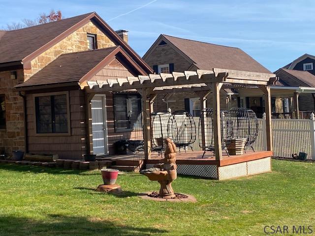 rear view of property featuring a wooden deck, a pergola, and a lawn