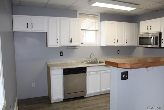 kitchen with appliances with stainless steel finishes, a paneled ceiling, sink, white cabinets, and dark wood-type flooring