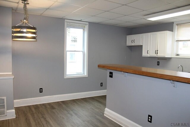 kitchen with hanging light fixtures, butcher block counters, a drop ceiling, and white cabinets