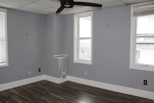 empty room with a drop ceiling, plenty of natural light, and dark hardwood / wood-style floors