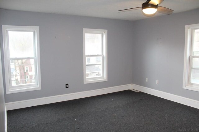 spare room featuring plenty of natural light, ceiling fan, and dark colored carpet