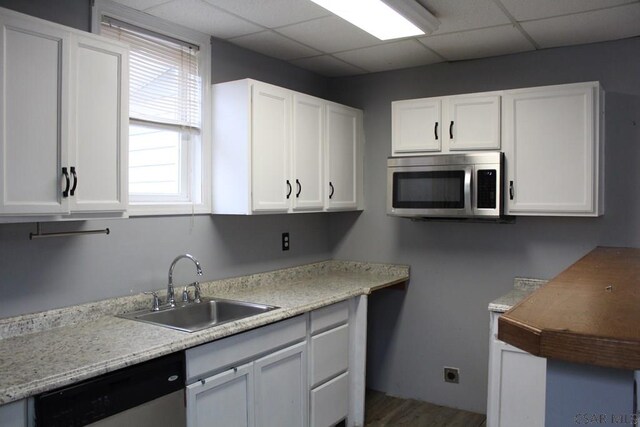 kitchen with stainless steel appliances, white cabinetry, sink, and a drop ceiling