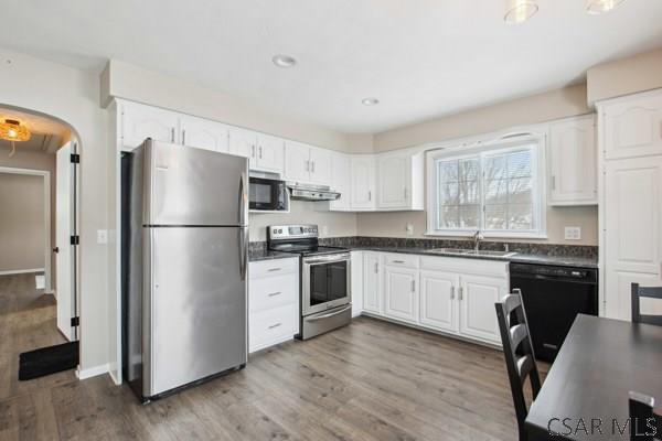 kitchen with sink, wood-type flooring, ventilation hood, appliances with stainless steel finishes, and white cabinets