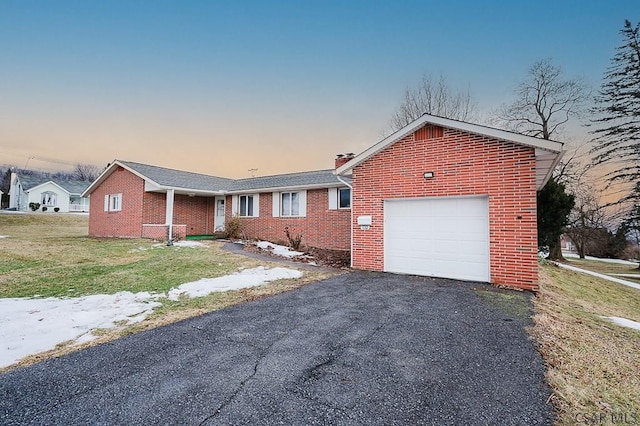 single story home with driveway, brick siding, a chimney, an attached garage, and a front yard