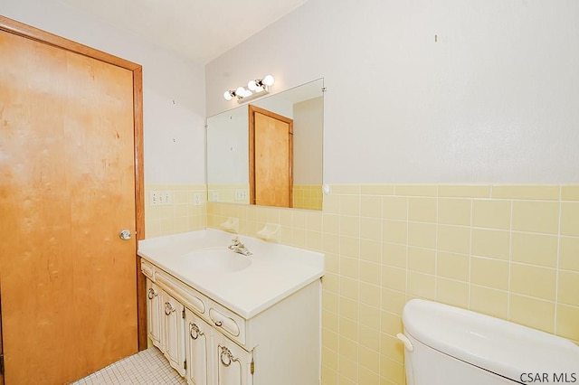 half bathroom with wainscoting, toilet, tile walls, and vanity