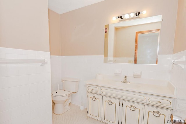 bathroom with a wainscoted wall, tile walls, toilet, vanity, and tile patterned floors