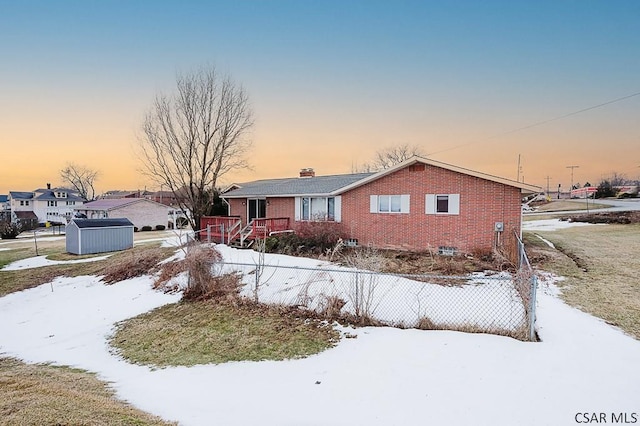 view of front of home with brick siding, a storage unit, fence, and an outbuilding