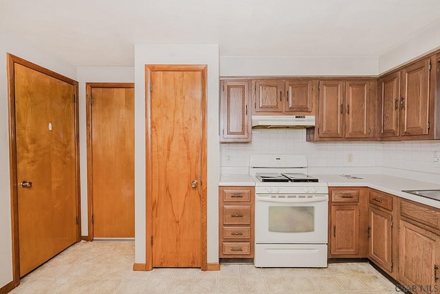 kitchen with white gas stove, backsplash, light countertops, and under cabinet range hood