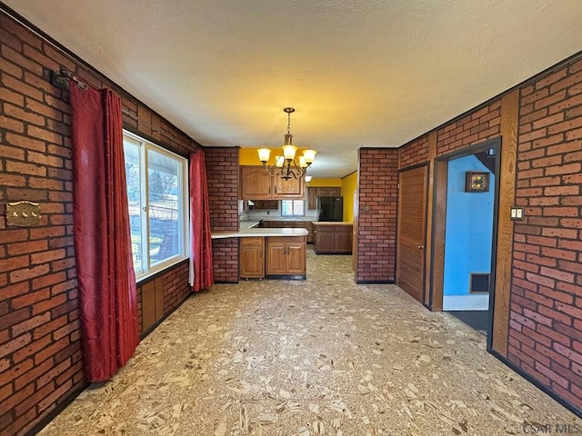 kitchen featuring brick wall, light countertops, a textured ceiling, a chandelier, and black fridge