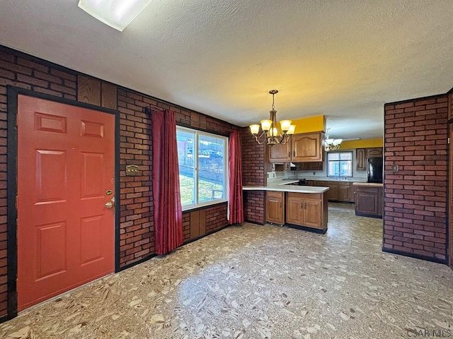 kitchen with a notable chandelier, black refrigerator, a peninsula, brick wall, and light countertops