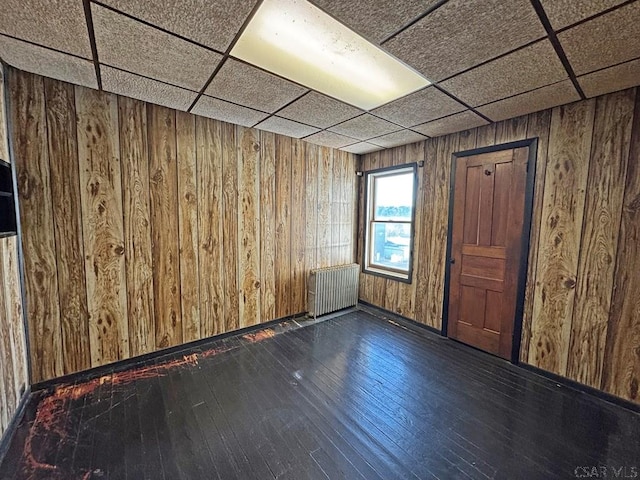 spare room featuring a paneled ceiling, radiator, wood walls, and dark wood-style flooring