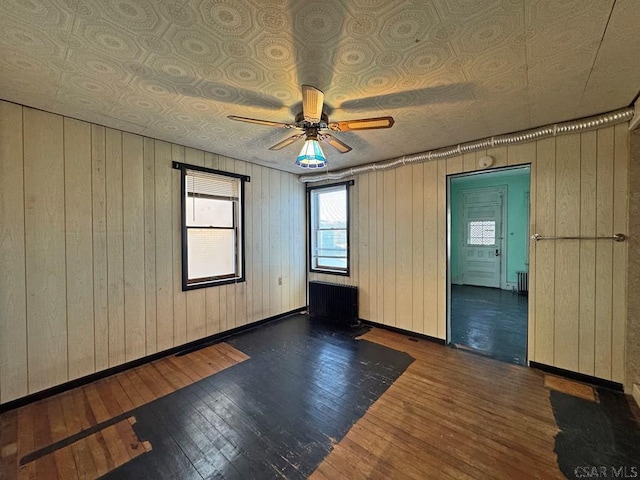 empty room featuring radiator, baseboards, wood-type flooring, and ceiling fan