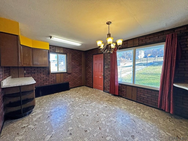 unfurnished dining area with a notable chandelier, brick wall, and a textured ceiling