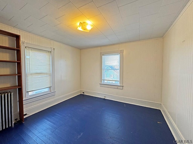 empty room featuring dark wood-type flooring, radiator, and baseboards