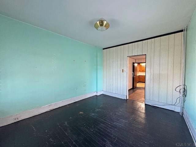 empty room with wooden walls, dark wood-style floors, and baseboards