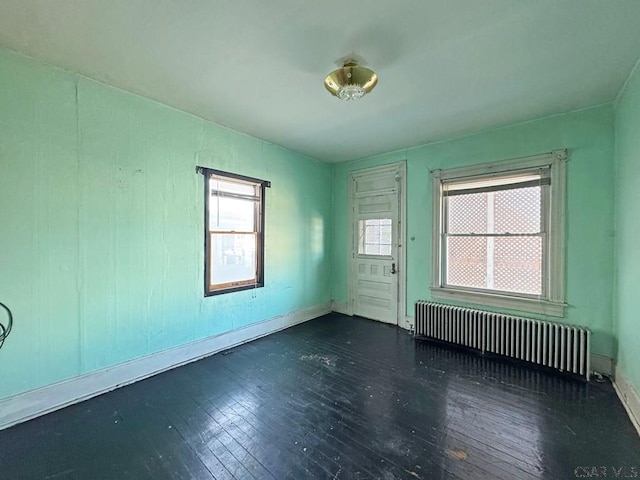 empty room with hardwood / wood-style flooring, radiator heating unit, and baseboards