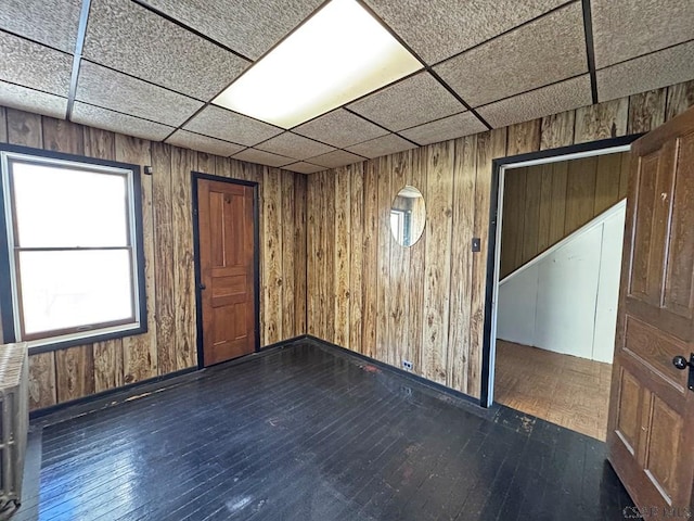 unfurnished room with wooden walls, dark wood-style floors, and a paneled ceiling