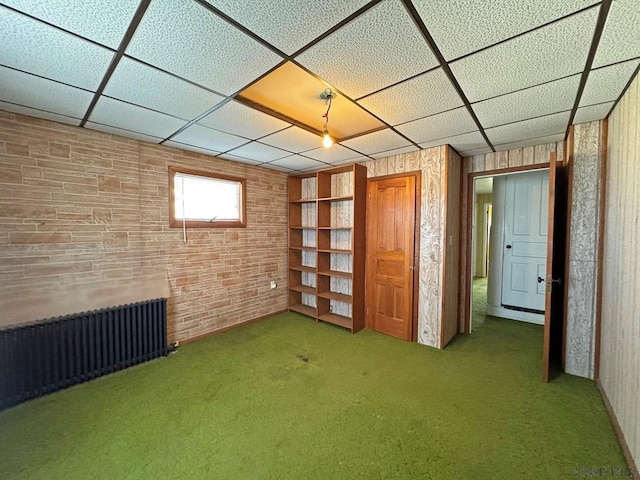 basement with a drop ceiling, carpet floors, and radiator heating unit