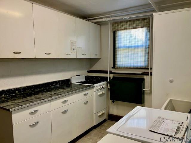 kitchen featuring white range with gas stovetop, dark countertops, and white cabinetry