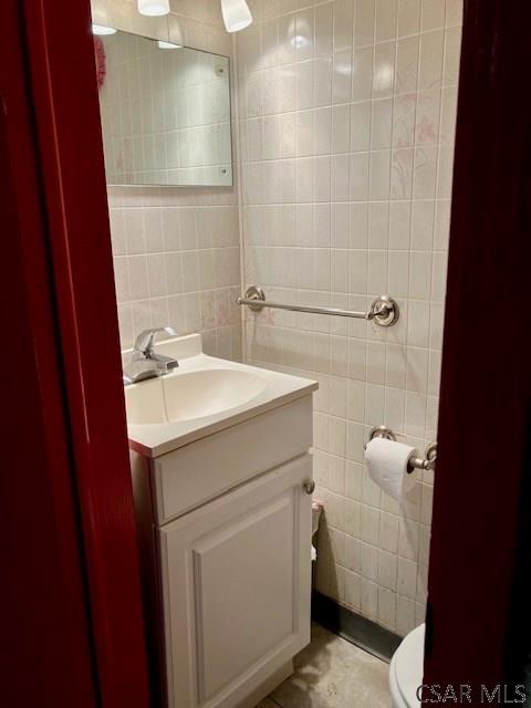 half bathroom featuring toilet, tile walls, and vanity