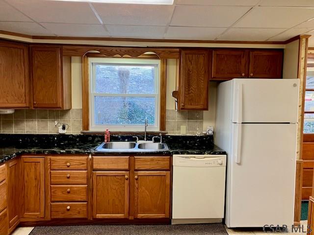 kitchen featuring tasteful backsplash, brown cabinets, white appliances, and a sink