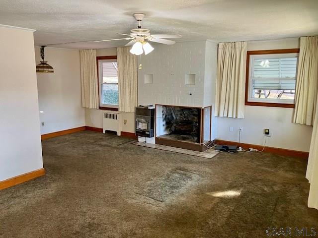 unfurnished living room with radiator, baseboards, carpet, a fireplace with flush hearth, and a ceiling fan