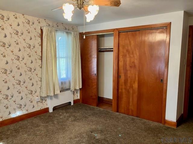 unfurnished bedroom featuring radiator, carpet flooring, wallpapered walls, baseboards, and ceiling fan