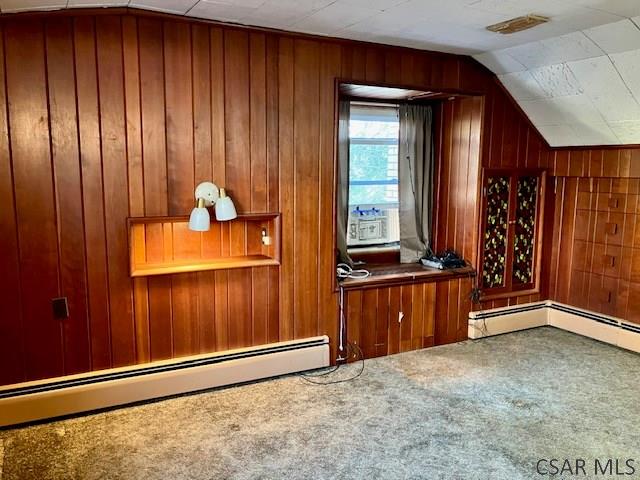 bonus room featuring vaulted ceiling, carpet flooring, wooden walls, and a baseboard radiator