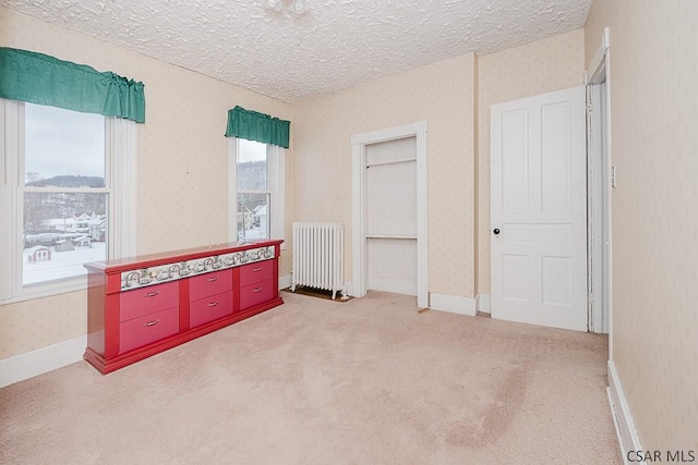 bedroom with light carpet, radiator heating unit, and a textured ceiling