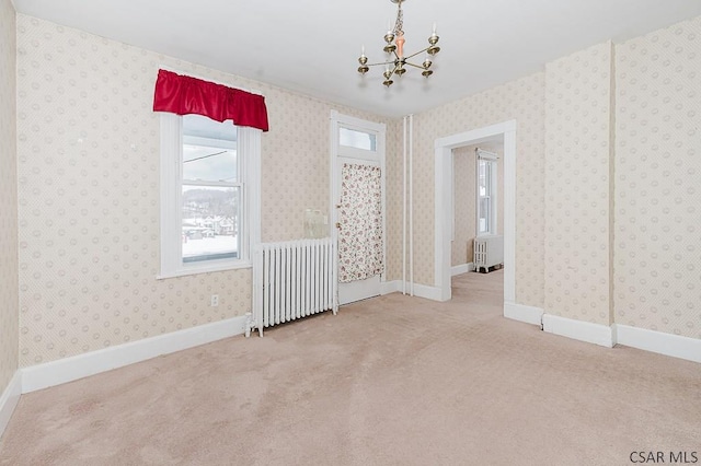 carpeted empty room featuring radiator heating unit and a notable chandelier