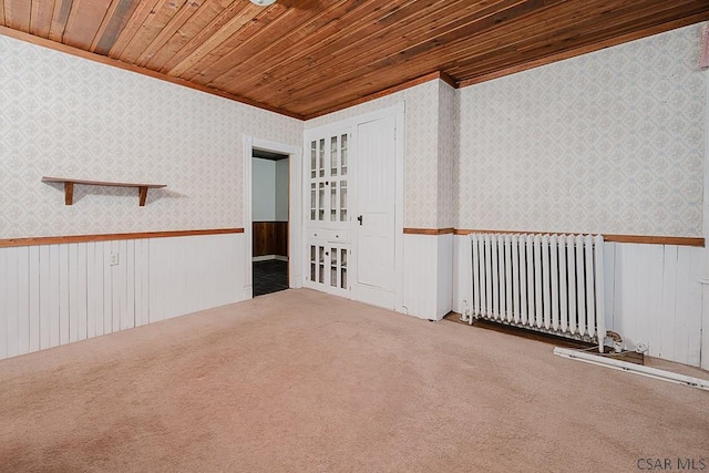 carpeted spare room featuring crown molding, radiator, and wooden ceiling