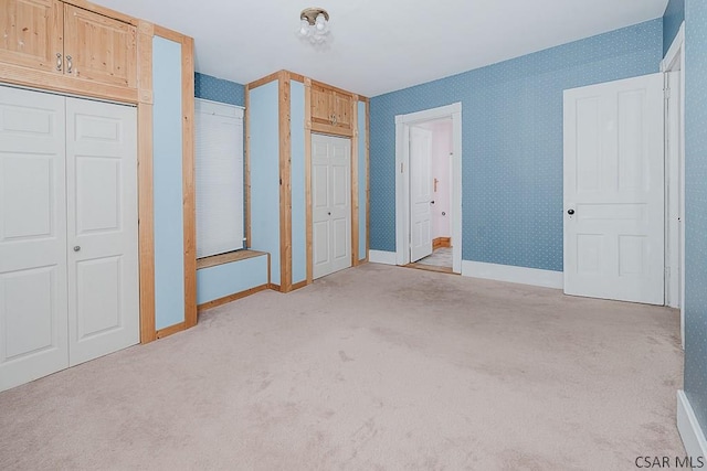 unfurnished bedroom featuring light carpet and multiple closets