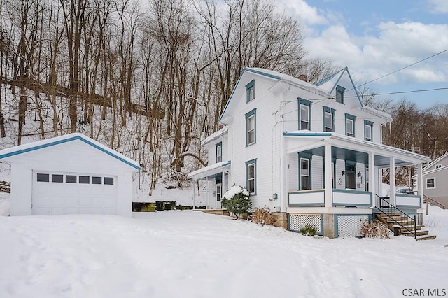 snow covered property featuring a garage, an outbuilding, and covered porch