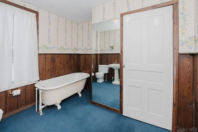 bathroom with a tub to relax in, wood walls, and toilet