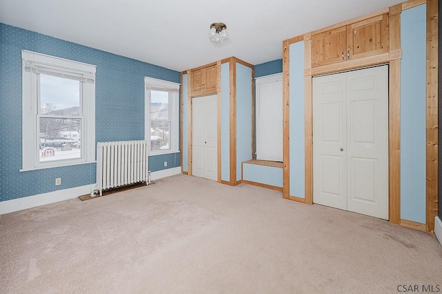 unfurnished bedroom with multiple closets, radiator, and light carpet