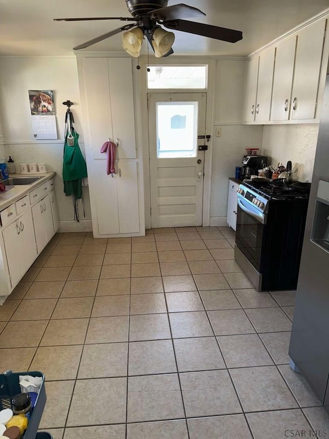 kitchen with light tile patterned floors, sink, ceiling fan, stainless steel gas range oven, and white cabinets