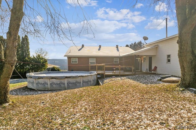 rear view of property featuring a covered pool, brick siding, and a deck