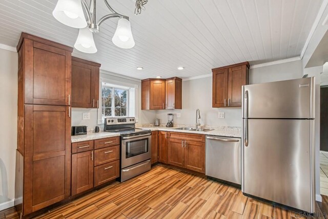 kitchen with appliances with stainless steel finishes, decorative light fixtures, sink, crown molding, and light hardwood / wood-style flooring