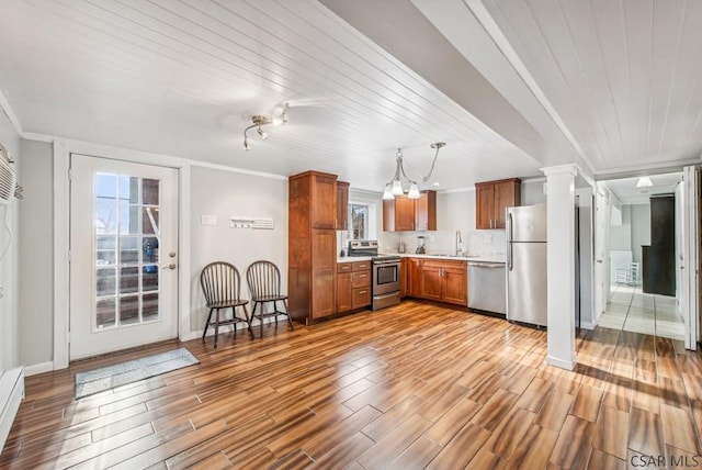 kitchen with brown cabinetry, appliances with stainless steel finishes, ornamental molding, light countertops, and a sink