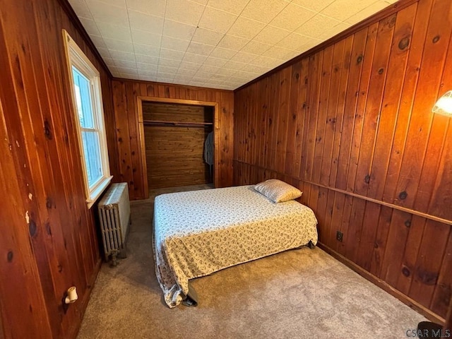 carpeted bedroom featuring radiator heating unit, wood walls, and a closet